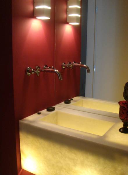 A pia iluminada e a parede vermelha s&atilde;o o destaque deste lavabo projetado por Andr&eacute; Martins. Repare que, para n&atilde;o ter que furar o espelho e para economizar espa&ccedil;o, as torneiras foram parara na parede lateral.