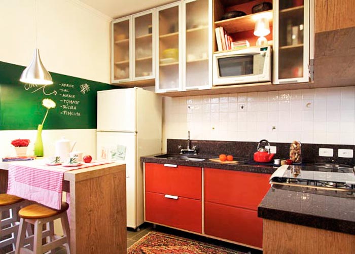 A cozinha projetada pela arquiteta Thais Lenzi Bressiani utiliza o vermelho no arm&aacute;rio e em diversos acess&oacute;rios . Na parede, uma tinta que imita lousa &eacute; utilizada para anotar recados e receitas. Para n&atilde;o pesar no ambiente, os arm&aacute;rios ganharam portas transl&uacute;cidas.