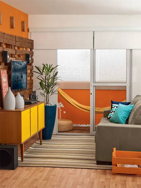 Rede em varanda min&uacute;scula. Um home theater instalado em um painel de paletes comp&otilde;e a sala com abertura para a varanda. O cuidado do arquiteto Gl&aacute;ucio Gon&ccedil;alves ao projetar o ambiente foi colocar persianas revestidas de blecaute na janela para que a claridade n&atilde;o atrapalhe na hora que rolar um filme. A rede otimizou o pequeno espa&ccedil;o do lado de fora e, dela, d&aacute; at&eacute; para assistir &agrave; televis&atilde;o.