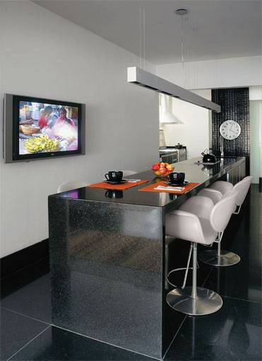 24 m&sup2;: Meio sala, meio cozinha, este ambiente gourmet no Rio de Janeiro nasceu em uma reforma promovida pelos arquitetos paulistas Antonio Ferreira Jr. e Mario Celso Bernardes. O propriet&aacute;rio do apartamento, um jovem m&eacute;dico que gosta de receber, pediu um balc&atilde;o comprido (4,40 x 0,80 m) que atendesse aos dois espa&ccedil;os, inclusive fazendo as vezes de mesa de refei&ccedil;&otilde;es em frente &agrave; TV. O material? O cl&aacute;ssico e neutro granito preto absoluto, o mesmo do piso, onde forma placas de 80 x 80 cm. Um pilar estrutural que precisou ser mantido foi disfar&ccedil;ado com pastilhas de porcelana pretas  o restante da &aacute;rea recebeu pintura branca. Rasgos na alvenaria ganharam prateleiras e conquistaram status de arm&aacute;rios para utens&iacute;lios.