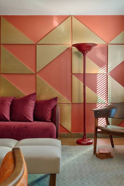 Esta sala, criada pela Melina Mundim, trabalha principalmente com tons terrosos e avermelhados, com exce&ccedil;&atilde;o das cadeiras ao fundo, dos bancos, do tapete e dos pain&eacute;is triangulares. A decora&ccedil;&atilde;o tamb&eacute;m possui uma influ&ecirc;ncia retr&ocirc;, como pode ser observado na lumin&aacute;ria de ch&atilde;o vermelha, nos formatos arredondados do sof&aacute; e das poltronas e na estampa geom&eacute;trica criada pelos pain&eacute;is dourados na parede.