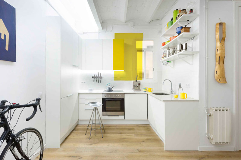 As paredes completamente brancas são subitamente recortadas por um retângulo amarelo. Além de iluminar a cozinha, ele faz com que ela pareça ainda maior.