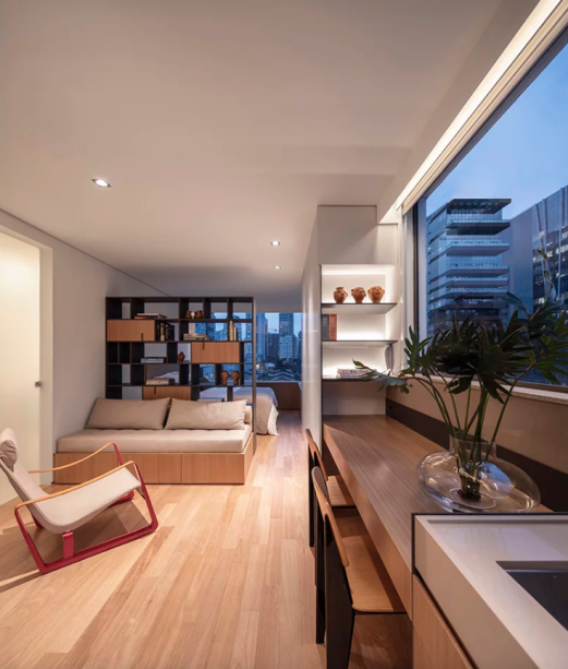 O desafio do plano compacto e estreito de 32 m² foi resolvido com a eliminação da varanda, incorporando-a ao apartamento para ganhar mais espaço e criar integração de maneira linear. Uma linha contínua de carpintaria foi projetada para otimizar ainda mais os espaços, com diferentes usos – a superfície da cômoda se estende e se transforma em armário, mesa e bancada da cozinha.