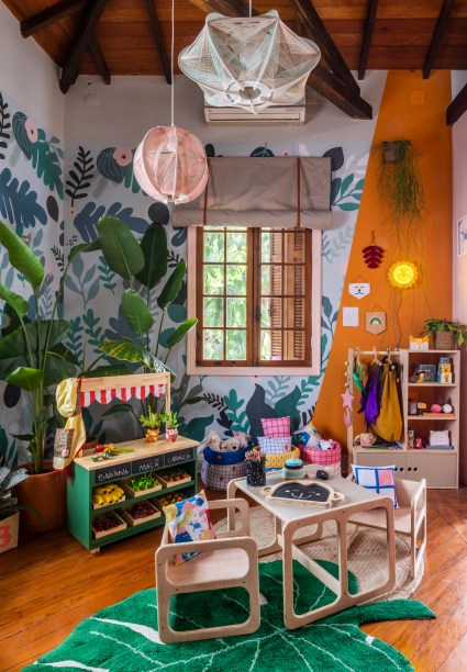 Brinquedoteca - Julia Varon Ferraz e Isadora Vaz da Silva Sousa, do Forma 011, Adot e Ateliê Materno. Um espaço totalmente dedicado para a diversão das crianças. De um lado, estão uma cozinha de madeira e um mini nicho sob medida para leitores pequeninos. De outro, um mercadinho natural com muitas plantas e frutas em madeira. Ligando as duas áreas, o painel “Flora” com estampa de folhagem.