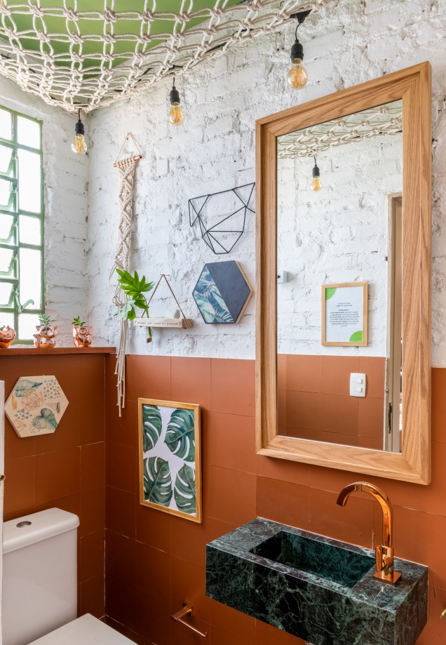 Lavabo In - Isabela Fraia Arquitetura. Os tijolos maciços originais foram mantidos e forrados com ladrilho hidráulico e adesivo em tom cobre. A bancada é esculpida em granito verde. No teto mora o charme do ambiente, uma trama de macramê cheia de plantas e bichinhos.