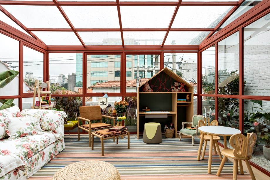 Varanda - Marina Linhares. Um gazebo de 39m², construído a partir de uma estrutura metálica e em vidro, explorando a luz natural e integrado ao paisagismo de Gabi Pileggi, do Jardineiro Fiel. Pensado para reunir a família em um momento de contemplação do horizonte, o espaço é pontuado por flores e plantas. O interior apresenta móveis confortáveis estofados com tecidos naturais e objetos de design. Uma estante com dois metros e formato de casinha abriga uma coleção de brinquedos.