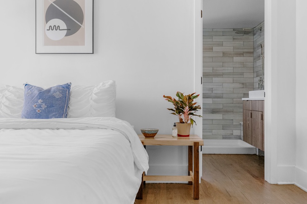limpeza-colchão Quarto com cores claras, roupa de cama branca e mesa lateral de madeira