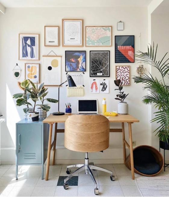 como-a-gente-mora-home-office-01 home office com cadeira e mesa em madeira. computador na mesa. Plantas em ambos os lados. Quadros diversos na parede