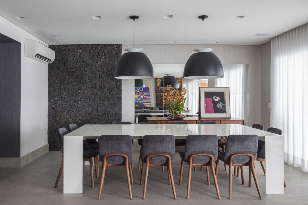 Sala de jantar com mesa de vidro branca e cadeiras com pernas de madeira e estofado cinza, com dois pendentes