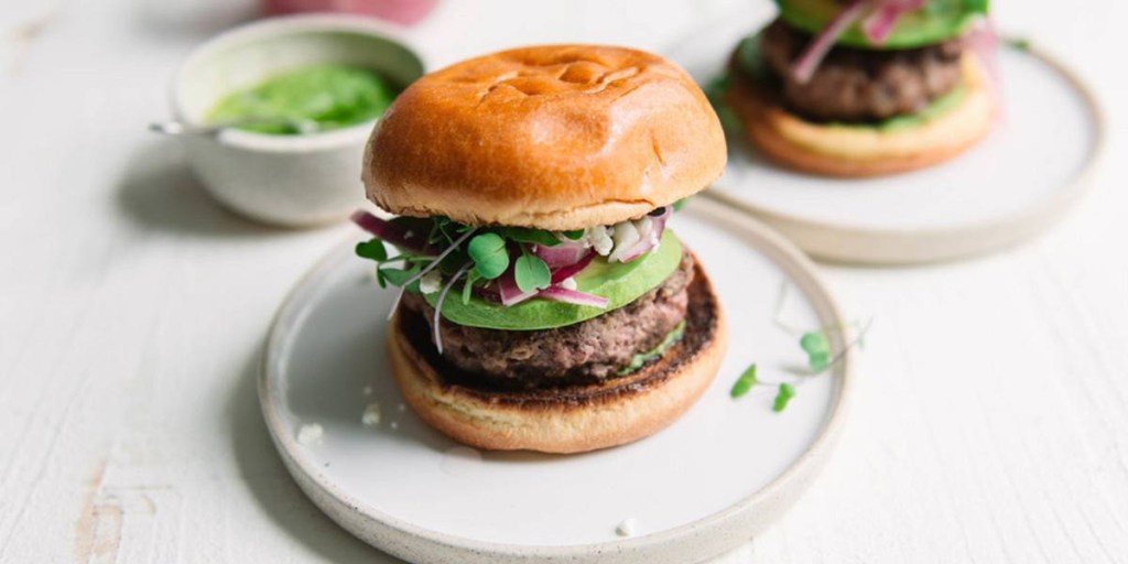 Hamburguer em prato de cerâmica clara com microverdes.