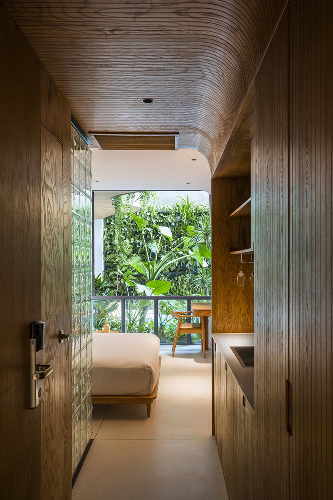 floresta-particular-varanda-parece-selva-casa.com-archdaily-ka-studio-hiroyuki-oki-26 Quarto com mobiliéario de madeira e rattan, materiais ecológicos, com uma cama branca e vista para a varanda com uma vegetação exuberante