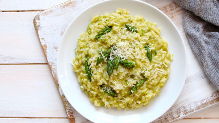 Prato com risoto amarelo em prato branco em mesa de madeira