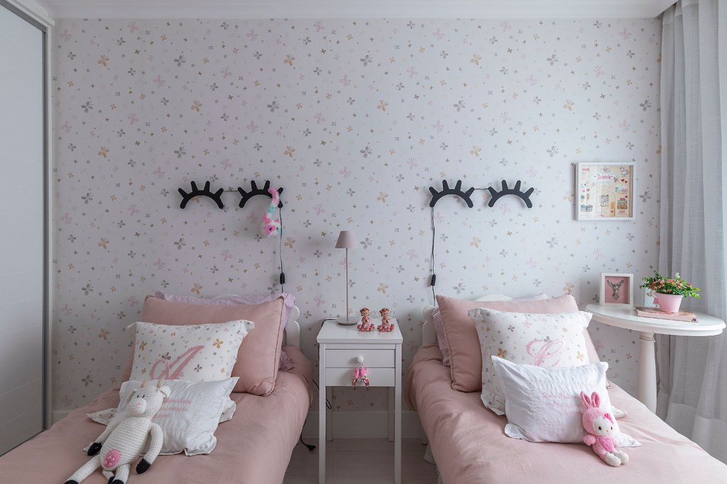 Quarto infantil, com duas camas com roupa rosa e luminárias sobre elas em formato de olhos fechados com cílios