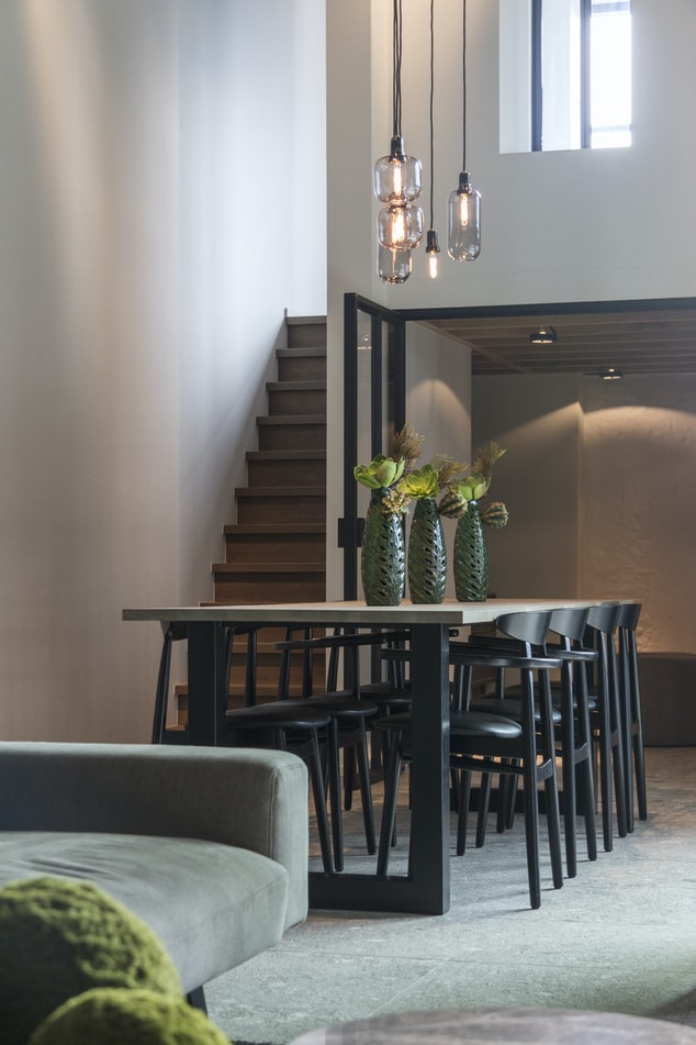 veja-solucoes-para-decorar-as-paredes-da-sua-casa-casa.com-5-unsplash-jean-philippe-delberghe Sala de jantar, com mesa de madeira e cadeiras pretas, com luminárias pendentes, vista da sala de estar, que tem um sofá verde
