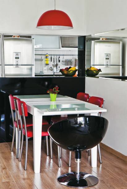 Um espelho cobre toda a largura da parede no canto de refei&ccedil;&otilde;es. A altura tamb&eacute;m tem sua raz&atilde;o: &eacute; id&ecirc;ntica &agrave; do v&atilde;o entre a cozinha e a sala. Na face vista da sala, o balc&atilde;o &eacute; revestido de um elegante laminado preto brilhante. Se desencostada da parede, a mesa recebe at&eacute; 8 pessoas.