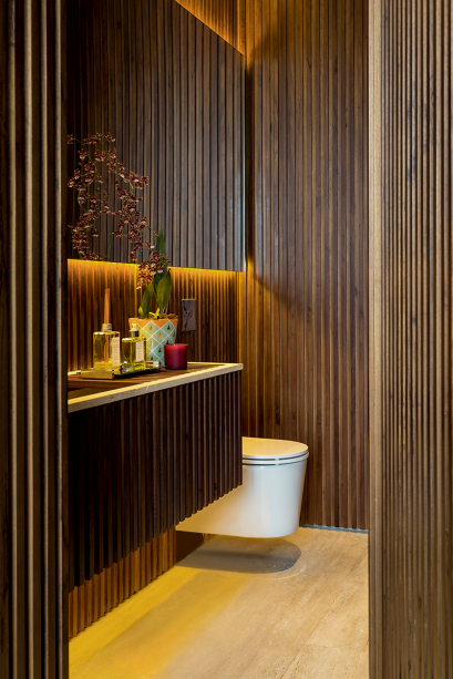 A madeira ripada nas paredes e na porta do arm&aacute;rio do lavabo criado pela designer de interiores Marina Linhares foi valorizada pela ilumina&ccedil;&atilde;o embutida com fitas de led 3 000 K (Lumini). Elas foram fixadas em cima e embaixo do painel superior destacado da parede, assim como na parte inferior do gabinete, com acionamentos independentes e dimeriz&aacute;veis.