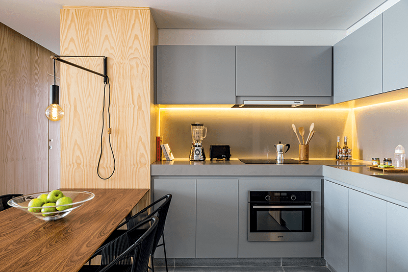 Demarcando os setores da cozinha, o arquiteto Gabriel Garbin usou em toda a extens&atilde;o dos arm&aacute;rios as fitas de led formando uma moldura na altura da vis&atilde;o. Plafons de led oferecem a ilumina&ccedil;&atilde;o geral necess&aacute;ria. Tudo da Lumini. Sobre a mesa, a pe&ccedil;a da Wall Lamps ganhou l&acirc;mpada de filamento de carbono.