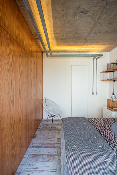 No quarto projetado pelos arquitetos Diogo Luz e Z&eacute; Guilherme Carceles, do escrit&oacute;rio Casa 100, o intuito foi valorizar a textura da laje de concreto. Para isso, usaram duas faixas de eletrocalhas, de 6 m cada uma, fixadas com bra&ccedil;adeiras met&aacute;licas. Dentro delas, colaram fita de led com temperatura de cor 2 700 K (Lustres Yamamura). Na lateral da cama, a lumin&aacute;ria (Tok&Stok) recebeu l&acirc;mpadas led comuns. Produ&ccedil;&atilde;o visual: Nuria Uliana.
