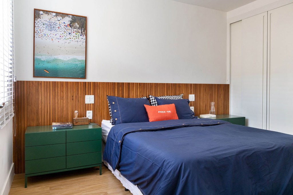 Quarto de casal com cabeceira de madeira ripada, roupa de cama azul e mesa lateral verde