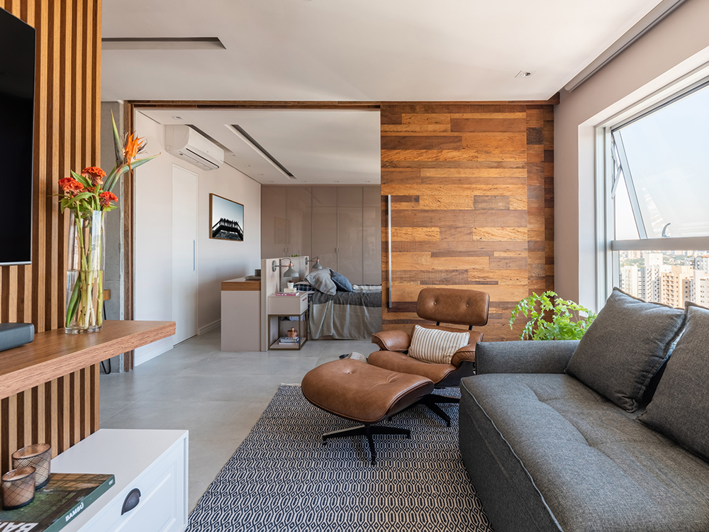 5 projetos com 5 soluções de arquitetura para espaços pequenos. Projeto de Studio Guadix. Na foto, sala de estar com divisória de correr, poltrona Eames, sofá cinza.