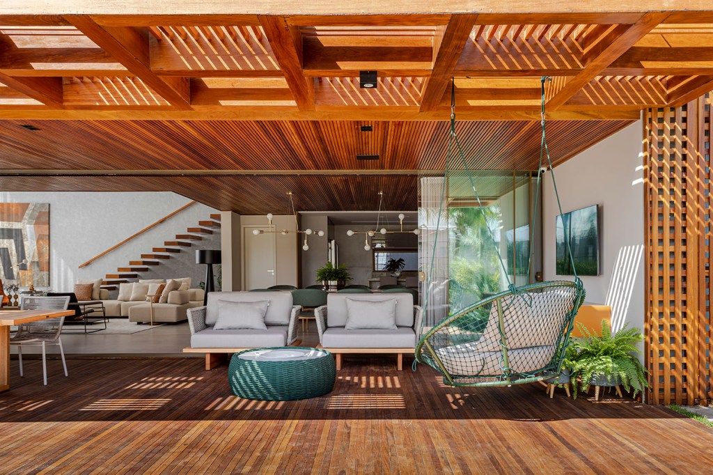 estilo-contemporaneo-guia-construcao-da-casa-muxarabi-na-bahia-casa.com-sidney-quintela-gabriela-daltro-20 Deque de madeira com mobiliário branco, com vista para a sala de estar, onde o teto também é de amdeira, e os móveis tem um tom de creme