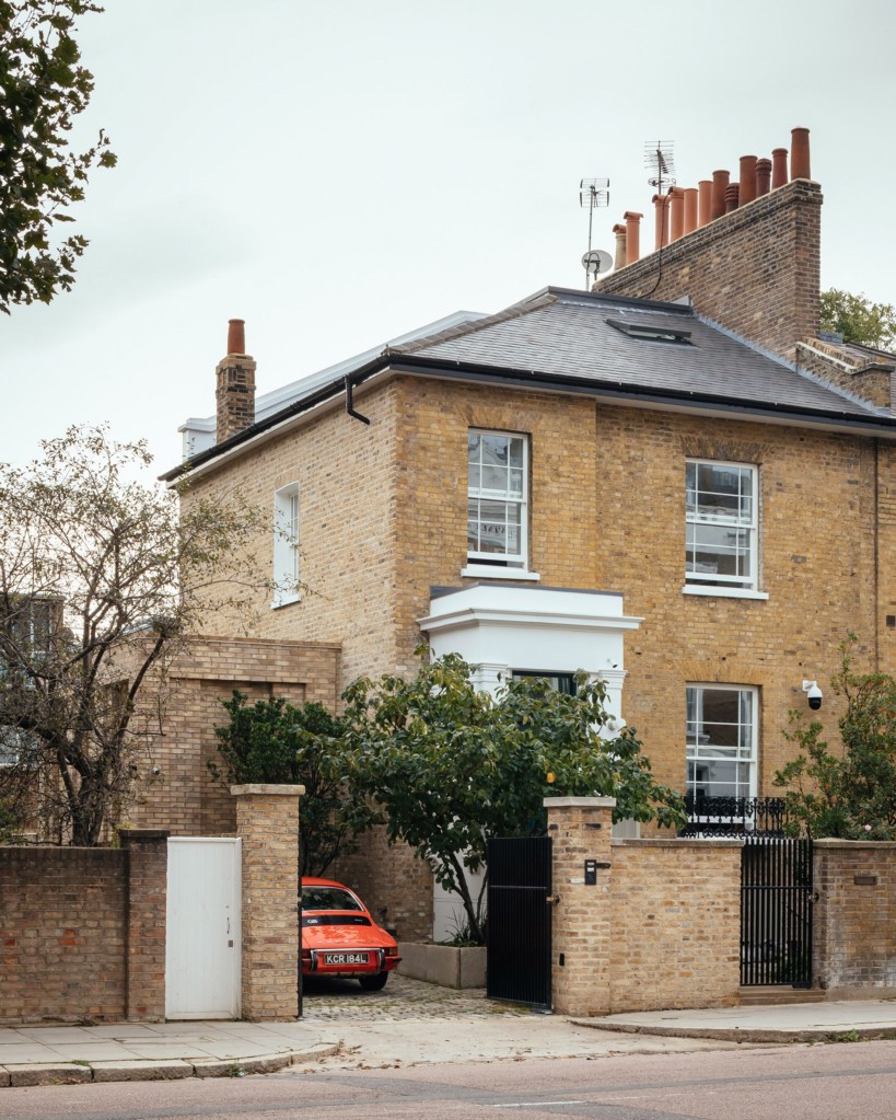 Fachada de casa vitoriana em Londres, com carro vermelho esportivo na garagem sob pergolado de plantas