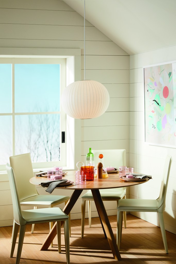 4-dicas-para-escolher-a-mesa-de-jantar-ideal-para-sua-casa-Herman-Miller-móveis-decoração-design-luminária Mesa de jantar de quatro lugares, sob luminária esférica branca, em uma sala bem iluminada por uma janela.