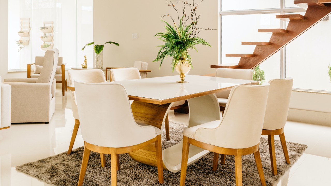 Sala de jantar com uma mesa de seis lugares, branca, com pés de madeira.