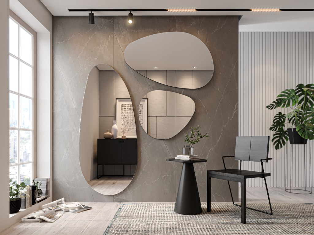 Sala com parede revestida em uma espécie de mármore acinzentado decorada por três espelhos recortados em formas irregulares arredondadas. Uma mesinha e cadeira minimalistas pretas arrematam a composição.