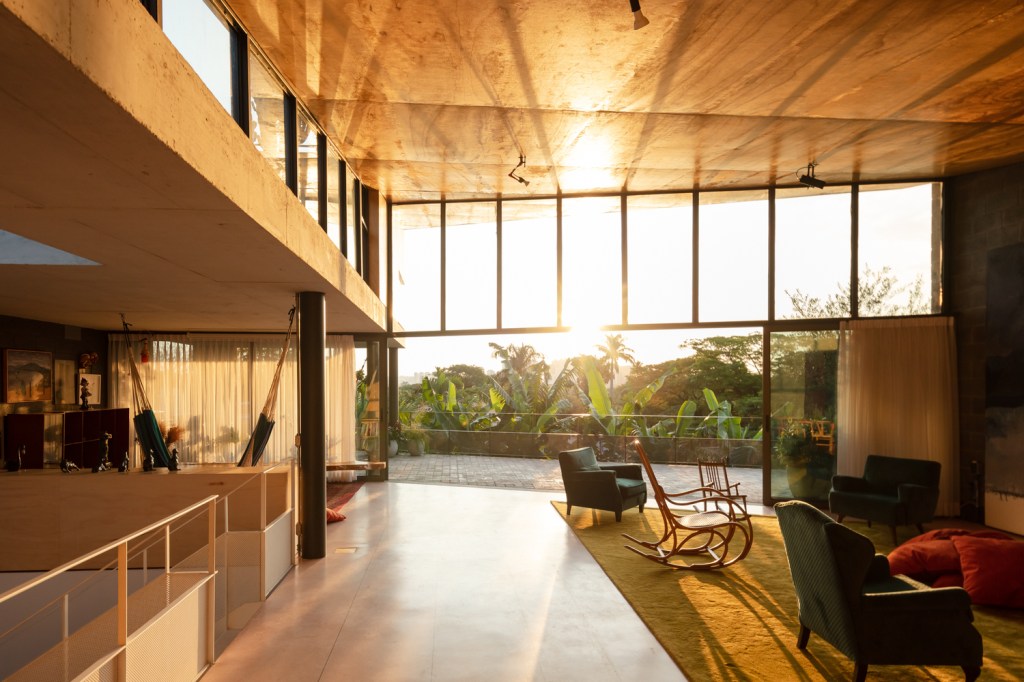 casa-sp-área-social-piso-superior-joão-morgado-sala-estar-entardecer-pe-direito-duplo Sala de estar ampla com painéis de vidro recebe luz do sol ao entardecer.