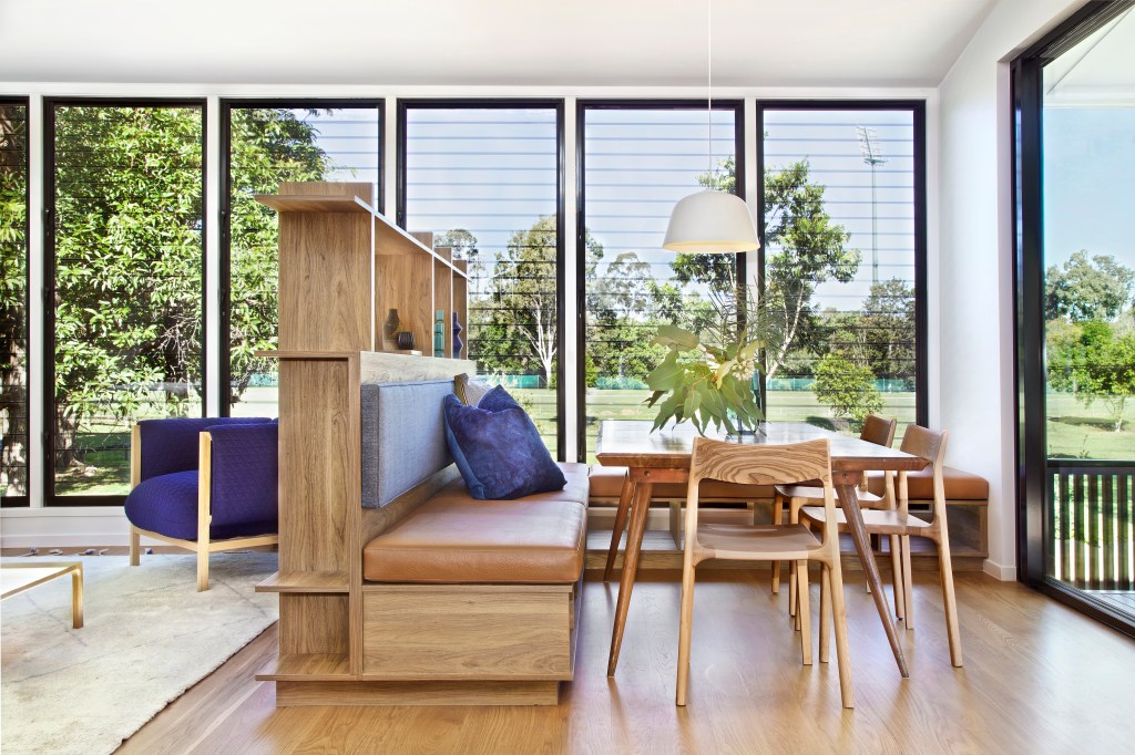 1-casa-de-180-2-transforma-rodape-em-estante-de-livros Sala com piso de madeira, sofá funcional cujo rodapé serve de estante e paredes de vidro