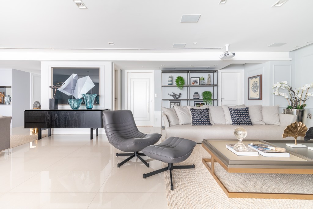 10-tons-neutros-sala-ampla-e-varandas-integradas-definem-este-ape Sala de estar com poltrona cinza e sofá branco, mesa de centro com vidro