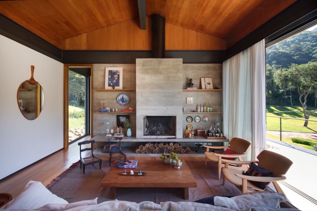 Sala de estar de casa de campo com teto de madeira, lareira, mesa de centro, sofá e poltronas