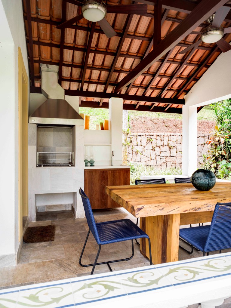 Varanda com mesa de madeira, churrasqueira branca e cadeiras azuis