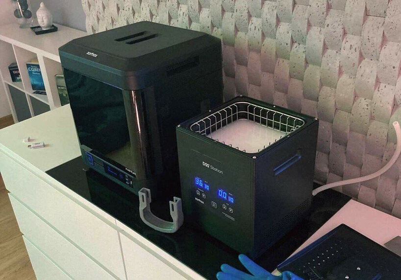 Veterinário-imprime-prótese-3D-para-cãezinhos-andarem (5) Impressora 3D e máquina para fazer molde sobre uma bancada. Os equipamentos tem formato de cubos.