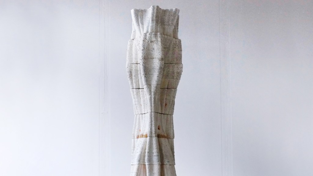10-materiais-que-podem-mudar-a-construção-divulgação-dezeen-coluna-de-micelio Foto mostra uma coluna em formato orgânico de cor cinza sobre fundo cinza claro.