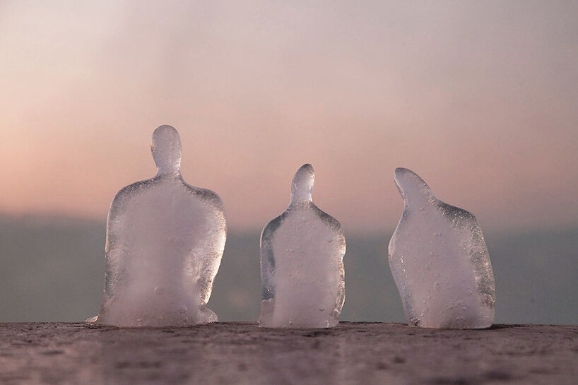 Pequenas esculturas de gelo derretendo de pessoas sentadas uma ao lado da outra de cabeças levemente baixas ao pôr do sol.