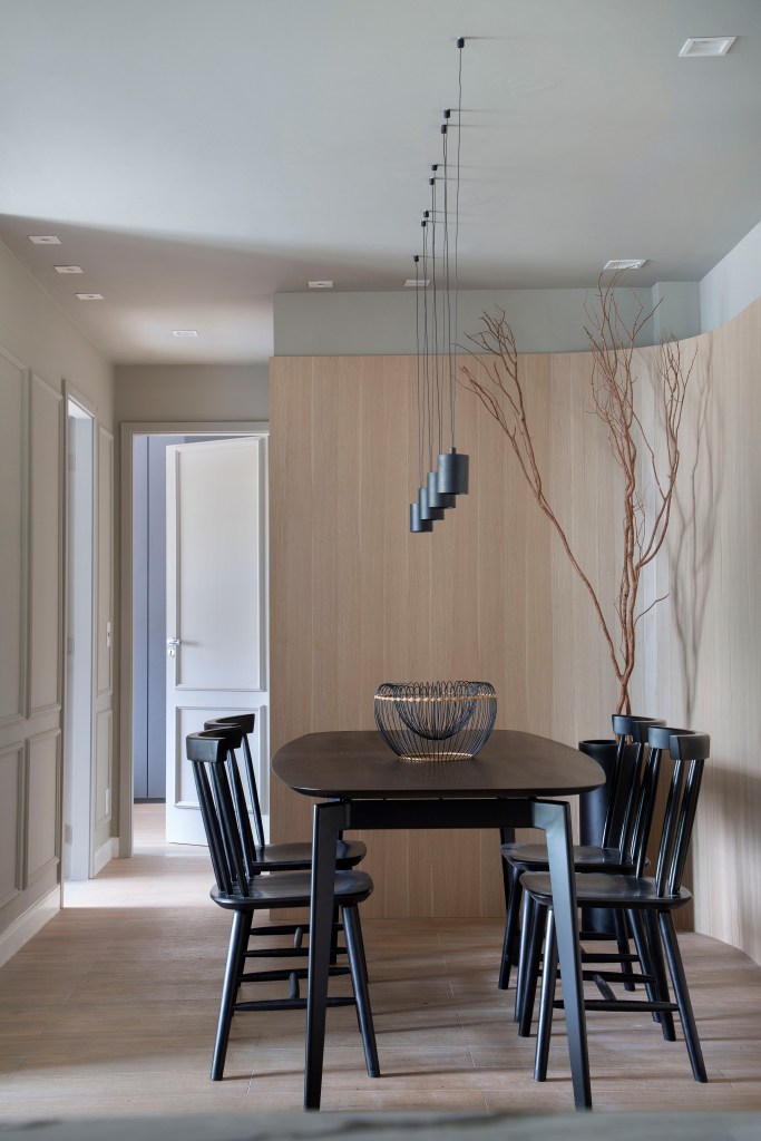 ape-95m-estilo-escandinavo-toques-industriais-up3arquitetura-foto-denilson-machado-sala-jantar-mesa-cadeira-pendente Sala de jantar com mesa e cadeiras pretas; painel curvo de madeira ao fundo; luminárias pendentes