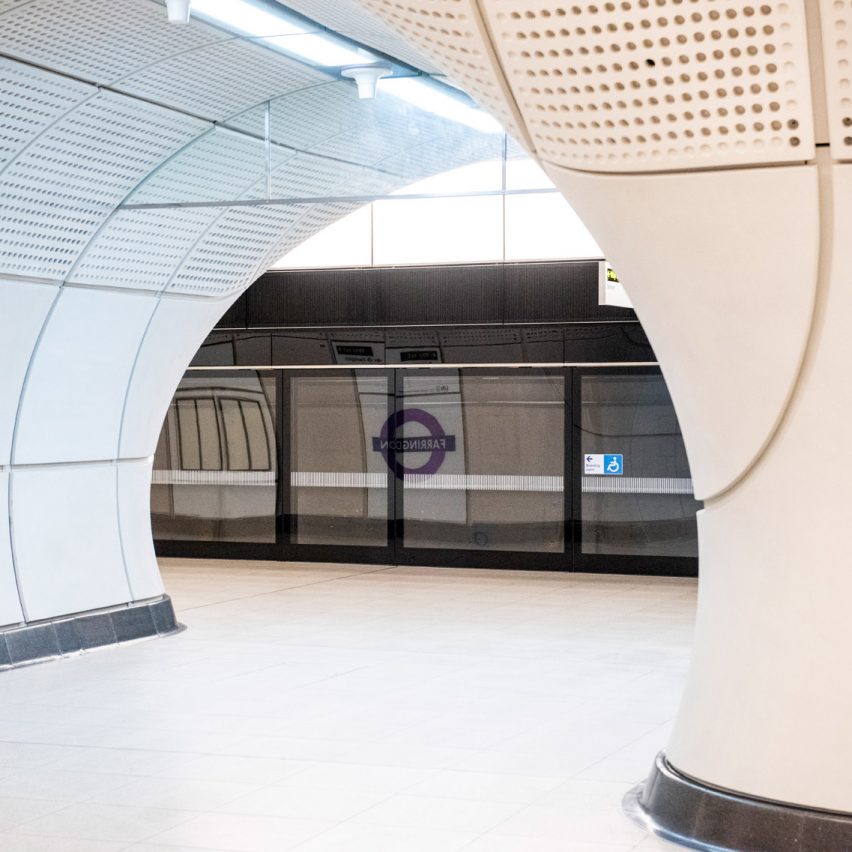 Foto mostra detalhe de paredes com teto curvo de estação de metrô, com trem ao fundo.