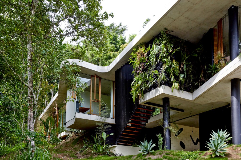 Vista da fachada com escada de acesso ao piso superior, em meio à floresta.