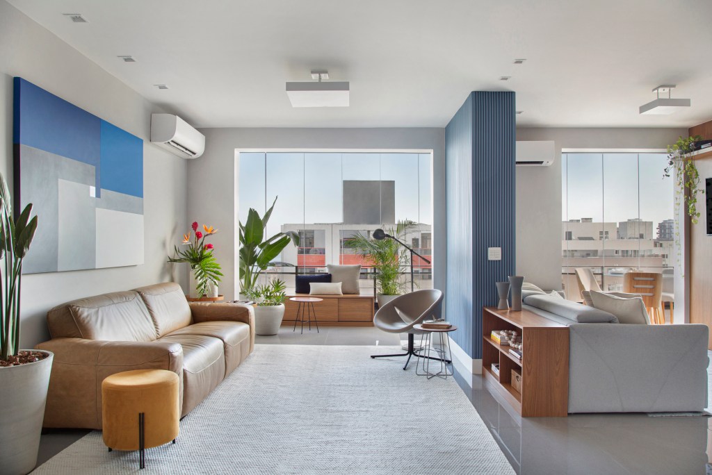 Sala de estar; parede de madeira azul; janela; poltrona neutra; sofá de couro