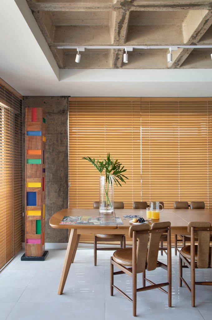 Sala de jantar com mesa e cadeiras de madeira; persianas.