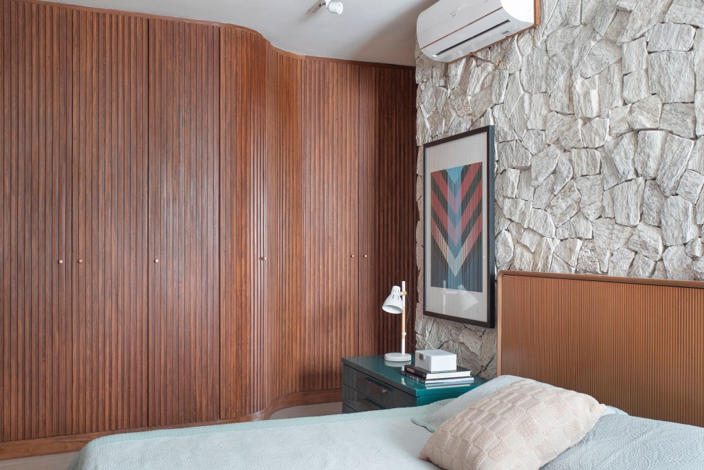 ape-160m-paineis-madeira-ripada-sofa-verde-design-nacional-roby-studio-arquitetura-10-quarto Quarto com cama de casal, parede de pedra e armários de madeira ripada.