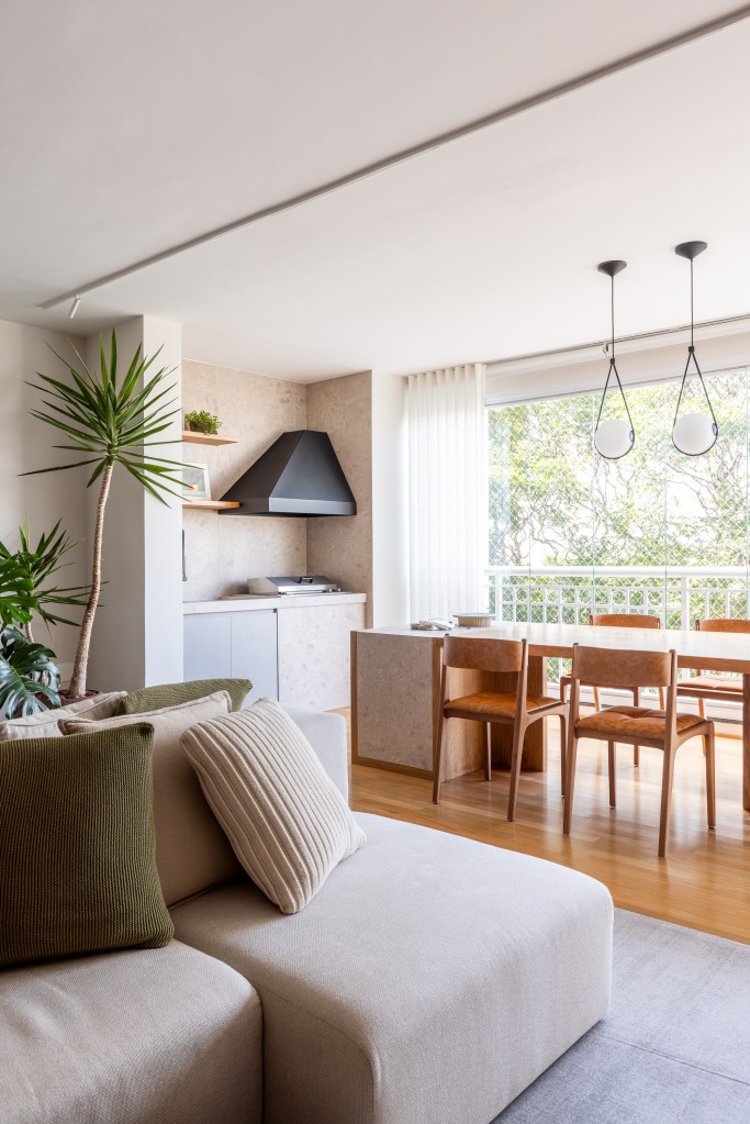 ape-integrado-140m-mesa-com-porcelanato-sofa-ilha-estudio-glik-interiores-13 Sala de estar integrada com varanda e churrasqueira; piso de madeira e mesa de madeira.