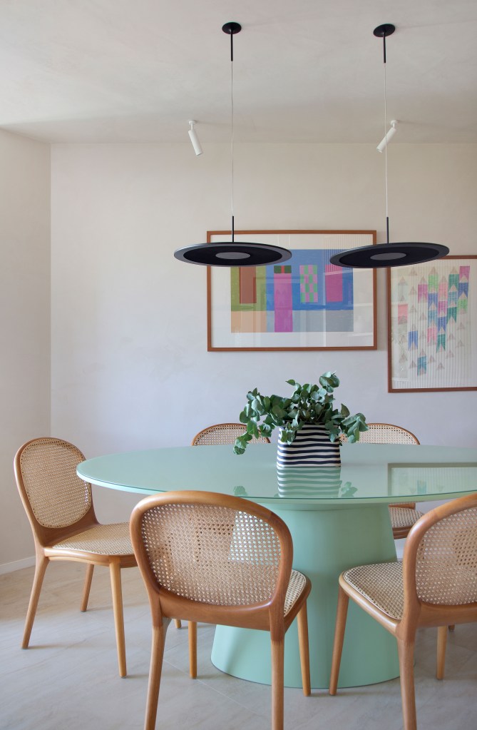 Sala de jantar com mesa redonda verde laqueada e cadeiras de madeira.