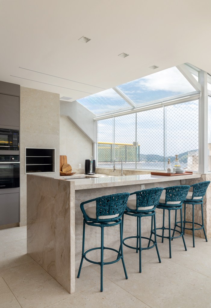 cobertura-estilo-urbano-no-primeiro-andar-e-praiano-no-segundo-nop-arquitetura-02-gourmet Área gourmet com janelas grandes, churrasqueira, bancada e banquetas.