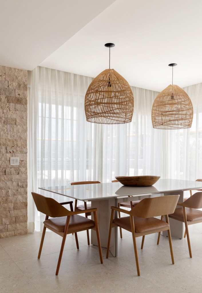cobertura-estilo-urbano-no-primeiro-andar-e-praiano-no-segundo-nop-arquitetura-07-jantar Sala de jantar com mesa de jantar, cadeiras de madeira, luminária de palhinha e cortina branca.