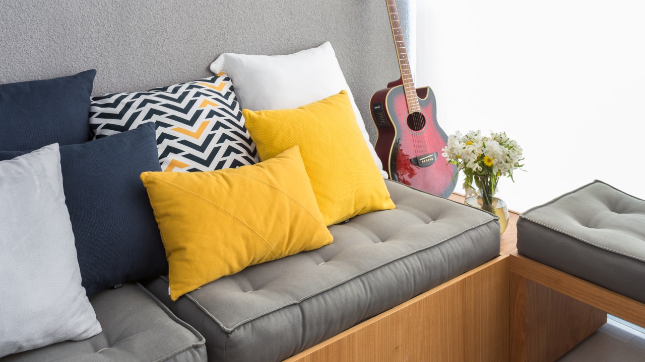 Futon cinza em varanda com almofadas amarelas.