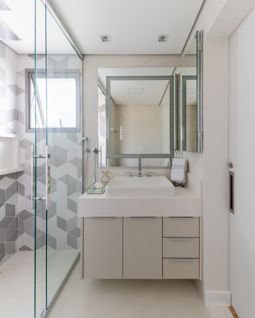 Banheiro com box de vidro e parede de azulejos geométricos brancos e cinzas.