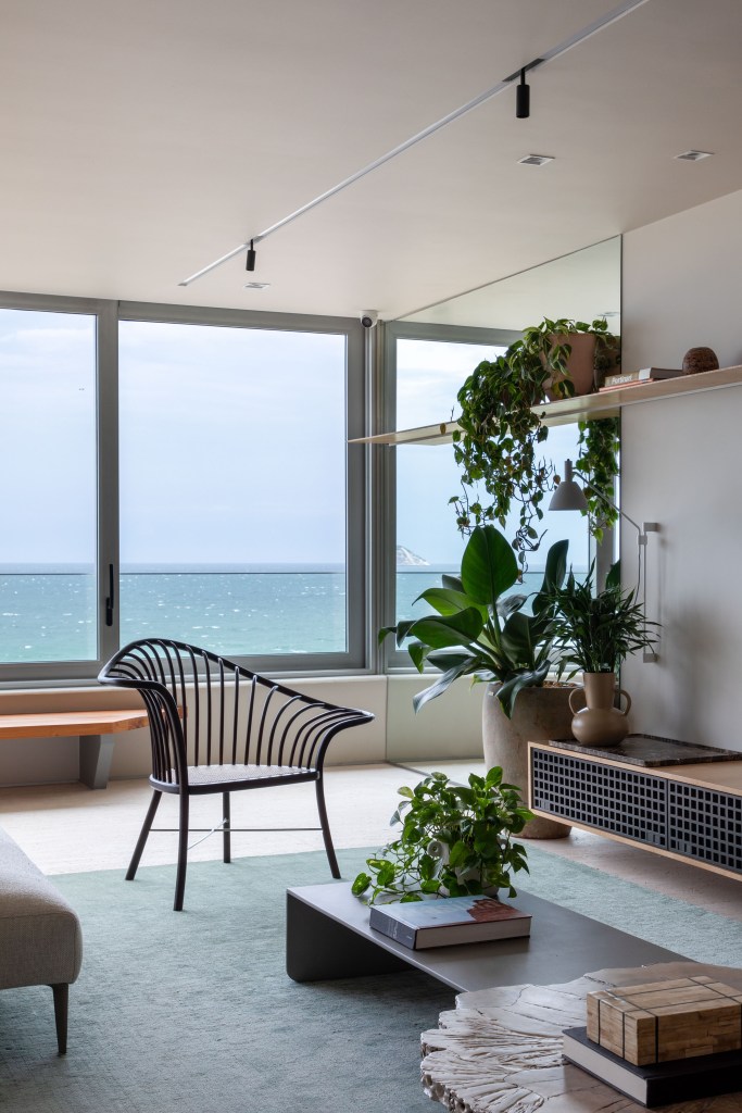reforma-cria-coworking-sala-intima-ape-320m-up3-arquitetura-03-sala-prateleira-plantas Sala de estar com janelas grandes, poltrona e prateleira com plantas.